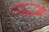 An angled view of the vintage Arak carpet, showcasing the ruby red field against the intricate floral border.
