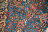 Close-up on the Kerman rug's full pile, showing scalloped spandrels and floral field.