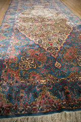 Angled view of a vintage Kerman runner showing the scalloped spandrel and floral field.