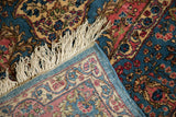 A folded corner contrasts the plush floral pile with the rug's fine, hand-knotted foundation.