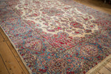 Dense floral sprays across the ivory field and sky blue cartouche border of the Kerman carpet.