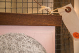 The rich walnut wood rod and twine hanger attached to the textured pink moon chart canvas.