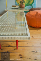 Detail of the handmade Mod Sled Table's intricate wood grid, glass top, and red mid-century leg.