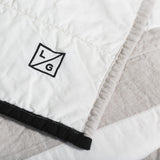 Louise Gray quilt corner detail with black logo, contrasting binding, and quilted white and tan cotton.