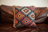 Antique Kilim pillow with multicolor geometric patterns, orange piping, and subtle repair.