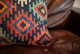 Geometric antique Kilim pillow with dark blue, rust, and teal pattern showing mended area.