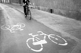 Black and white street photograph of a biker near cycle lane markings.