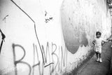 Melissa Dilmaghani Florence street photograph: child by a graffiti wall showing 'BAMBINI'.