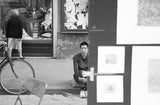 Black and white Florence street portrait, a man looks out, framed by blurry art.