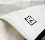 Louise Gray quilt detail with black embroidered LG logo and black trim on white cotton.