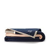 Folded Louise Gray Quilt No. 3 showing navy, peach, and tan layers with brand logo.