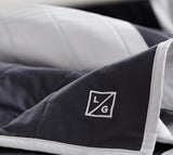Folded Louise Gray quilt corner with white embroidered LG logo and crisp white binding.