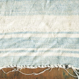 Textured indigo and white striped textile detail with frayed edge on rustic wood.