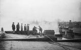 Antique black and white image of men operating early firefighting equipment on a roof.