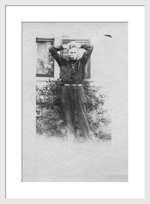Late 1910s black and white photograph of a boy posing with hands behind head.