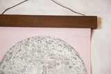 Close view of the walnut rod securing the pink cotton canvas moon chart.