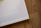 Detail of the white frame's mitered corner, showing slight chipping.