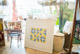 Large geometric photograph with blue and yellow blocks in a white frame, displayed in a bright shop.