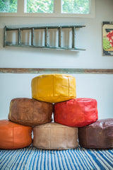 Stack of colorful distressed leather Moroccan poufs with stenciled fleur de lis motifs.