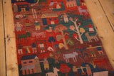 Pictorial folk art scenes with people, animals, and houses on a rustic red and deep teal Tibetan runner.
