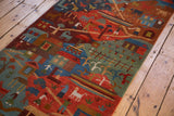 Vibrant hand-knotted pictorial folk art runner with houses, figures, and animals.