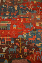 Angled close-up of plush pile Tibetan folk art rug, featuring carved figures in madder red and indigo.
