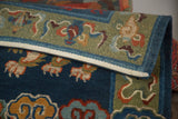 Folded hand-knotted Tibetan rug revealing plush indigo blue field, sage border, and natural dye Fu Dog motifs.
