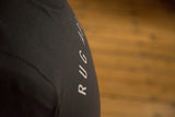 Side view of the white block lettering on the sleeve of a charcoal Rug Addict t-shirt.