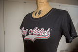 Retro 'Rug Addict' graphic on a charcoal t-shirt with white contrast stitching.