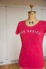 Profile view of the watermelon red Rug Addict t-shirt with fine contrast stitching.