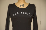Arched white Rug Addict block lettering on a women's black long sleeve shirt.