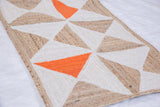 Handmade Rosie rug's braided geometric design in natural jute, white, and vivid orange.