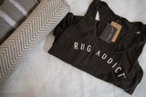 Gunpowder grey Rug Addict tank top with its hang tag, styled next to a rolled herringbone rug.