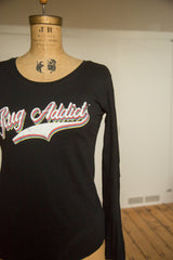 The black Rug Addict long-sleeve t-shirt with colorful retro script, shown from an angle.