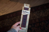 Bergamo Rug Bookmark with deep blue, terra cotta, and light blue traditional pattern, white fringe.