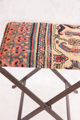 Intricate patterns of the antique Persian rug fragment footstool top, featuring rich red, blue, and gold tones.