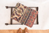 Antique Persian Doroksh rug fragment on a dark industrial folding footstool base.