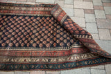 Partially rolled vintage Kurdish Bijar rug displaying its repeating Mir motif and distinctive laleh abassi border.