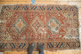 Antique Heriz rug showing geometric triple diamond medallions, serrated border, and worn copper field.