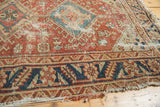 Antique Heriz rug's navy serrated leaf border and geometric patterns with visible wear.