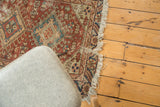 Corner of an antique Heriz rug, highlighting its geometric patterns in copper, navy, and beige with frayed fringe.