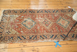Antique Heriz rug showing navy, beige serrated leaf border, copper field, and tattered edge.