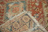 Tattered fringe, worn pile, and red-blue geometric patterns on an antique Heriz rug corner.
