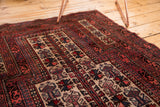 Detail of vintage Belouch rug's geometric boteh borders and plant motifs in reds and ivory.
