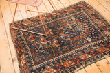 Geometric indigo, brick red, and ivory patterns of a hand-knotted Shirvan rug, with tattered edge.