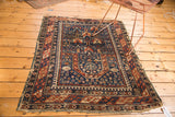 Vintage Shirvan rug's bottom corner, displaying tattered fringe and geometric indigo and brick red border.
