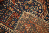 Folded corner of vintage Shirvan rug, showing geometric blue, red, ivory pattern and tattered foundation.
