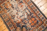 Antique Caucasian rug's geometric tangerine, navy, and ivory gul motifs with hard distress.