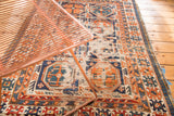 Close detail of antique Caucasian rug: distressed geometric gul motifs in tangerine, charcoal, ivory.