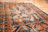 Antique Caucasian rug's distressed tangerine and blue gul motifs, with exposed foundation.